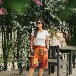 May include: A white short-sleeved crew neck t-shirt paired with knee-length patchwork cargo shorts featuring various shades of orange, brown, and green fabric panels, an elastic drawstring waistband, and multiple side pockets.