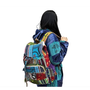 May include: A multi-colored patchwork backpack with a blue, green, red, yellow, and orange design. The backpack has a flap with a zipper closure and a drawstring closure. The backpack is being worn by a person with long black hair.