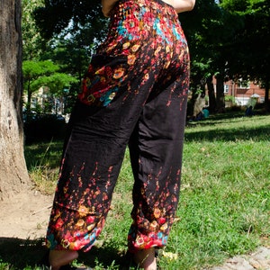 May include: Black pants with a floral print in shades of red, blue, and yellow. The pants have an elastic waistband and a loose, flowing fit.