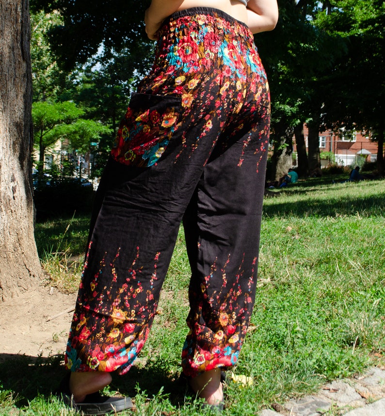 May include: Black pants with a floral print in shades of red, blue, and yellow. The pants have an elastic waistband and a loose, flowing fit.
