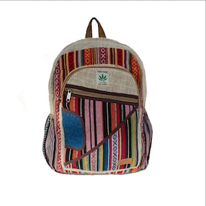 May include: A multi-colored hemp backpack with a large pocket on the front. The pocket has a brown zipper and a small patch with the text "PURE HEMP THE TRUE HEMP MADE IN NEPAL".