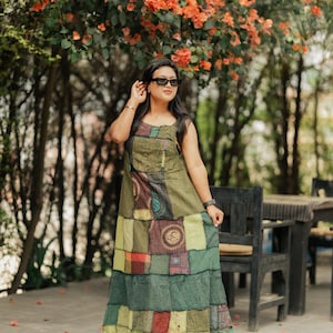 May include: A patchwork maxi dress in shades of green, brown, and red. The dress features a sleeveless design and a mix of patterned and solid fabric squares. The woman is wearing sunglasses and standing outdoors near a table and chairs.