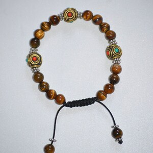 May include: A brown tiger's eye beaded bracelet with silver and gold accents. The bracelet has three decorative beads with red and turquoise accents. The bracelet has a black cord with a sliding knot for adjusting the size.