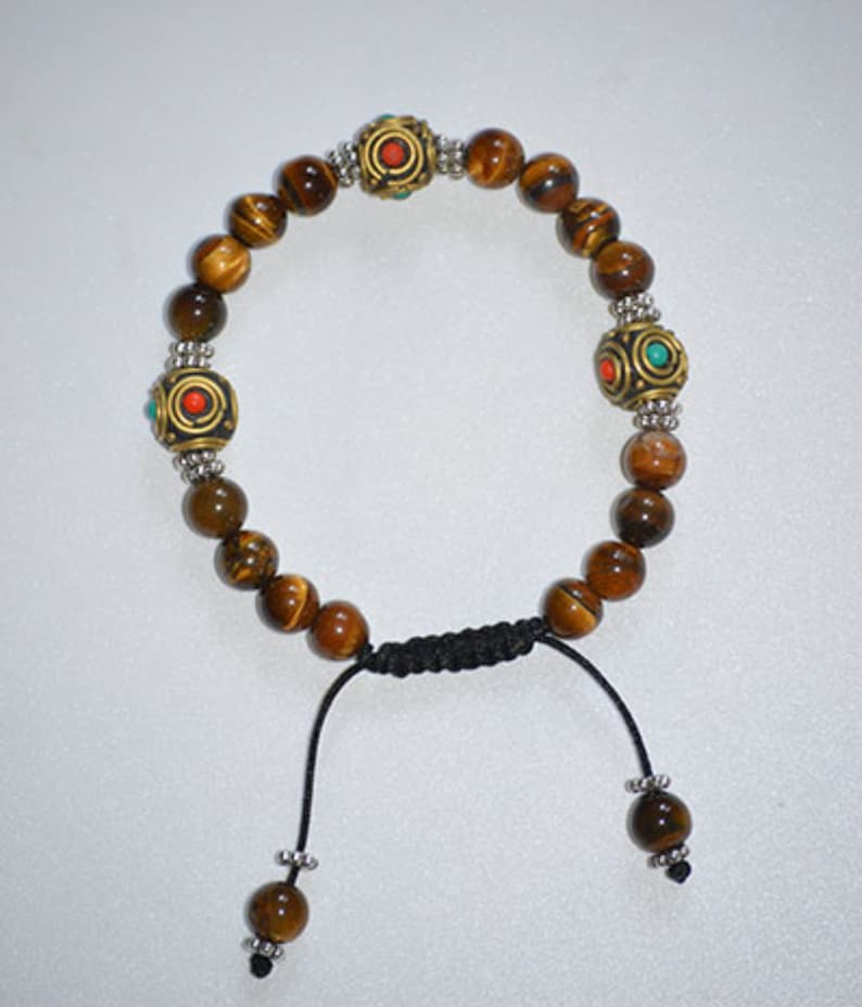 May include: A brown tiger's eye beaded bracelet with silver and gold accents. The bracelet has three decorative beads with red and turquoise accents. The bracelet has a black cord with a sliding knot for adjusting the size.