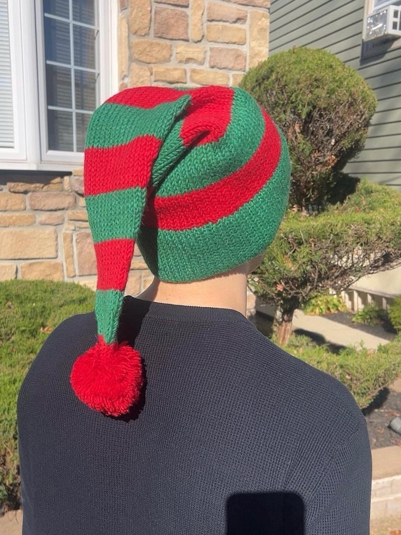 K&ouml;nnte beinhalten: Eine gr&uuml;n-rot gestreifte gestrickte Elfenm&uuml;tze mit einem roten Bommel am Ende der langen, spitzen Spitze.