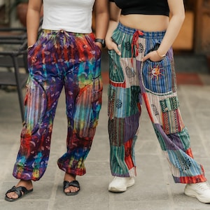 May include: Two pairs of loose-fitting trousers with elastic waistbands and drawstring closures. One pair features a vibrant tie-dye pattern in shades of blue, red, and purple. The other pair displays a multi-coloured patchwork design with stripes.