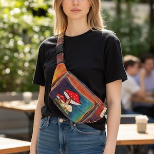 May include: A colorful fanny pack with a mushroom design. The bag has a rainbow-colored background and a strap with a geometric pattern. The person is wearing a black t-shirt and blue jeans.