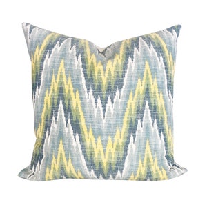 May include: Square decorative pillow with a zigzag pattern in shades of blue, yellow, and green. The pillow has a soft, textured appearance, suitable for adding a pop of color and pattern to any living space. The pillow is a square shape.