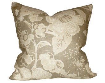 May include: Square decorative pillow with a floral pattern. The pillow features large, cream-colored flowers and foliage against a tan background. The fabric has a textured appearance, adding depth to the design.