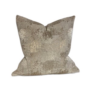 May include: A decorative throw pillow with a beige and gold abstract pattern. The pillow is made of a soft, textured fabric.