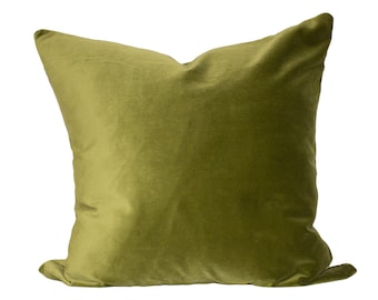 May include: A square, olive-green velvet pillow. The pillow has a soft, plush appearance and is set against a white background. The fabric has a subtle sheen, and the pillow is slightly crumpled, suggesting comfort.