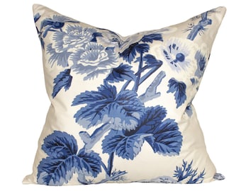 May include: Square throw pillow with a cream background and a large blue floral pattern. The design features detailed blue flowers and leaves, creating a classic and elegant look. The pillow is a decorative accent for a bed or sofa.