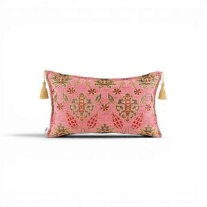 May include: Pink rectangular cushion with an elaborate floral design in green, red, and gold. The cushion features a gold tassel at each end, enhancing its appeal. A decorative item for the home.