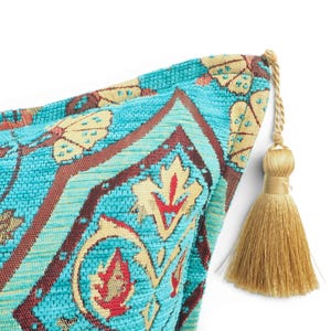 May include: A decorative throw pillow corner featuring a vibrant turquoise fabric with a woven pattern in shades of cream, brown, and red. The corner is finished with a single, long, light gold-colored tassel attached by a twisted cord.