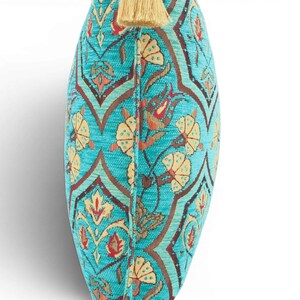 May include: A turquoise throw pillow featuring a repeating pattern of stylized yellow flowers and dark brown geometric lines. The pillow has a textured fabric surface and is finished with a single light beige tassel attached to the top center edge.