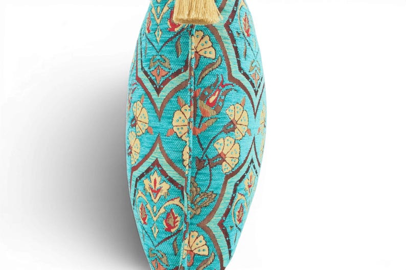 May include: A turquoise throw pillow featuring a repeating pattern of stylized yellow flowers and dark brown geometric lines. The pillow has a textured fabric surface and is finished with a single light beige tassel attached to the top center edge.
