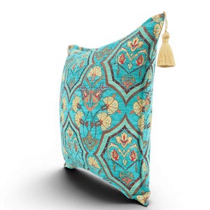 May include: A square throw pillow featuring a vibrant turquoise background with a repeating pattern of cream-colored floral motifs outlined in dark brown. The pillow is accented with a single beige tassel attached to the top corner of the fabric.