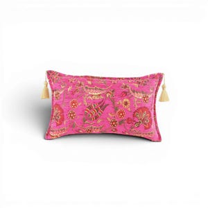 May include: A rectangular throw cushion in a vibrant hot pink fabric featuring a repeating floral and botanical pattern in shades of red, green, and gold. The cushion is finished with a decorative beige tassel attached to each of the two side corners.