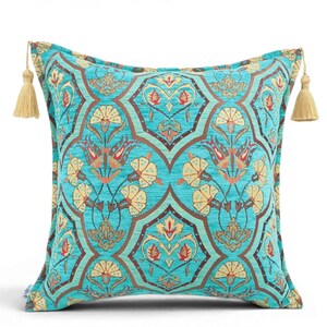 May include: A square throw pillow in a vibrant turquoise fabric featuring a repeating dark brown geometric lattice pattern filled with stylized floral motifs in shades of cream, red, and orange. The pillow is finished with beige tassels.