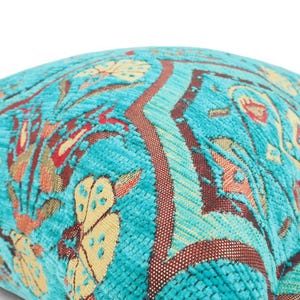 May include: A square throw pillow featuring a vibrant turquoise velvet base with a woven pattern of stylized flowers and geometric shapes in shades of cream, orange, and deep red. The fabric has a textured, raised pile finish throughout.