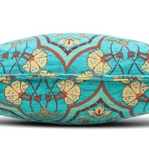 May include: A rectangular throw pillow featuring a vibrant turquoise fabric base with a repeating pattern of cream-colored floral motifs and dark brown geometric lines. The pillow has a visible piped edge seam running horizontally across the center.