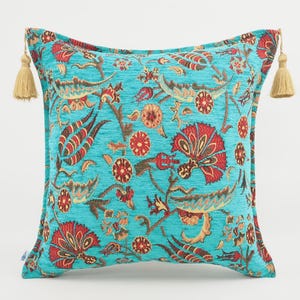 May include: A turquoise blue throw pillow with a floral pattern in shades of red, orange, and brown. The pillow has tassels on each corner.