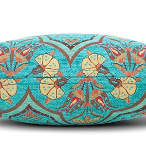 May include: A rectangular throw pillow featuring a vibrant turquoise background with a repeating woven pattern of stylized yellow flowers and reddish-brown tulip-like motifs. The fabric has a visible textured weave throughout the entire surface.