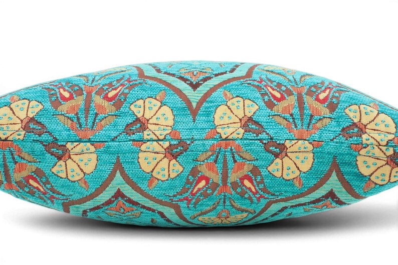 May include: A rectangular throw pillow featuring a vibrant turquoise background with a repeating woven pattern of stylized yellow flowers and reddish-brown tulip-like motifs. The fabric has a visible textured weave throughout the entire surface.
