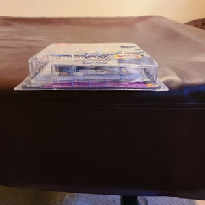 May include: A clear plastic package containing a Spider-Man action figure. The package has a purple and white background with the words "Spider-Man" printed in red and blue. The action figure is visible through the plastic and is wearing a red and blue suit.