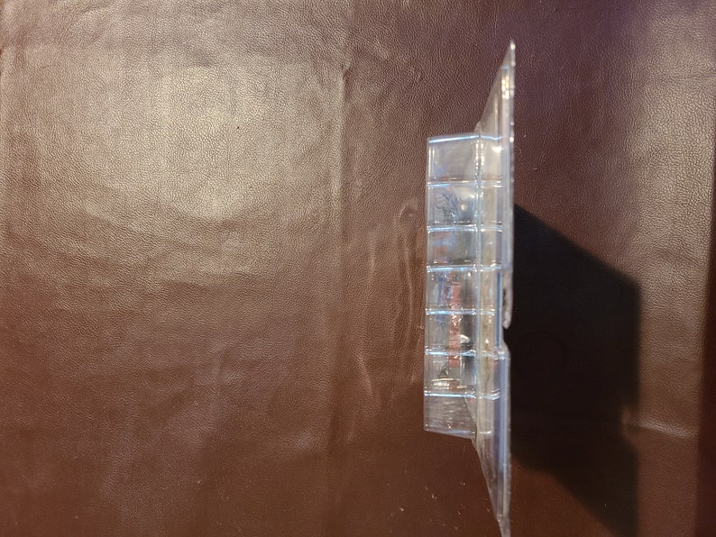 May include: A clear plastic blister pack containing a small toy figure. The figure is partially visible and appears to be made of plastic.