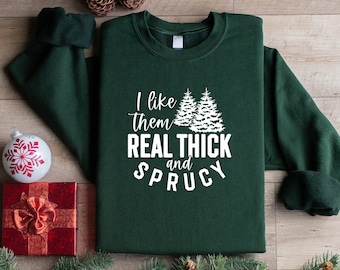 Può includere: Una felpa verde scuro con una grafica bianca che dice "I like them REAL THICK and SPRUCY" con due alberi di Natale bianchi stilizzati.