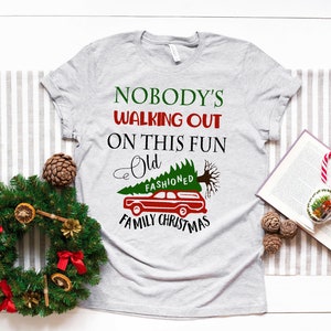 May include: A grey t-shirt with the text "Nobody's Walking Out On This Fun Old Fashioned Family Christmas" and a cartoon image of a car with a Christmas tree on top.