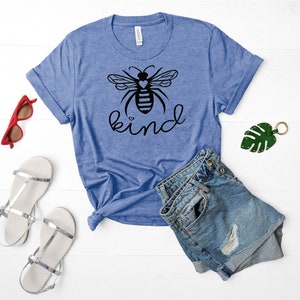 May include: A blue t-shirt featuring a black bee graphic and the word "kind" printed on it. The bee has a small heart on its body.