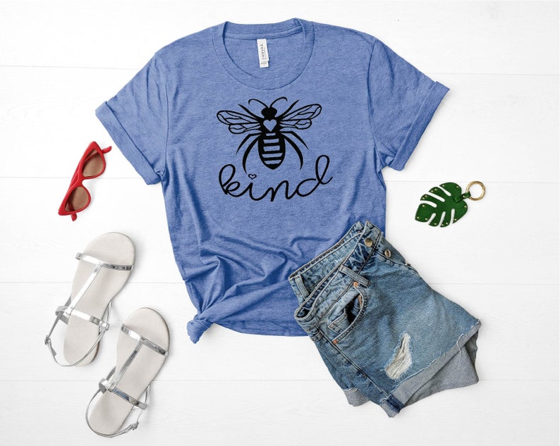 May include: A blue t-shirt featuring a black bee graphic and the word "kind" printed on it. The bee has a small heart on its body.