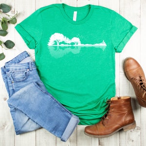 May include: A green t-shirt with a white graphic of a guitar silhouette with trees reflected in the water. The graphic is a reflection of a guitar with trees in the background.