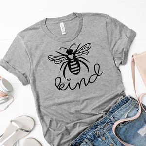 May include: Grey t-shirt featuring a black bee graphic and the word "kind" written in cursive. The bee has a small heart on its body.