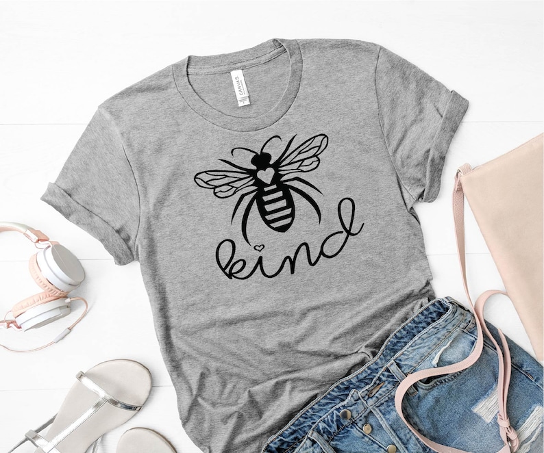 May include: Grey t-shirt featuring a black bee graphic and the word "kind" written in cursive. The bee has a small heart on its body.
