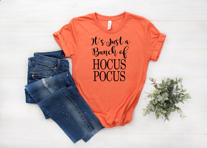 Puede incluir: Camiseta naranja con texto negro que dice "It's Just a Bunch of Hocus Pocus".