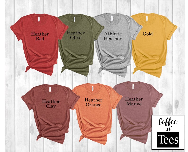 Puede incluir: Un conjunto de diez camisetas en varios colores jaspeado, incluyendo rojo, oliva, gris, dorado, arcilla, naranja y malva. Cada camiseta tiene un color diferente y presenta el texto "Heather" seguido del nombre del color.