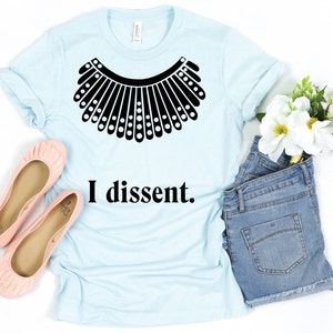 May include: A light blue t-shirt with a black graphic of a judge's collar and the text "I dissent."