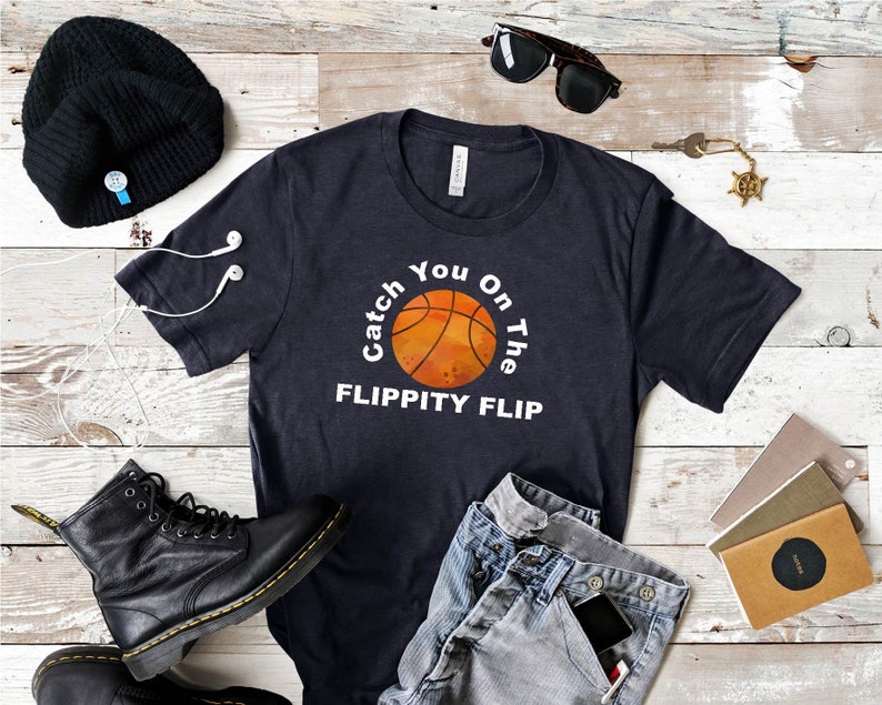 May include: A navy blue t-shirt with a white graphic of a basketball with the text "Catch You On The Flippity Flip".