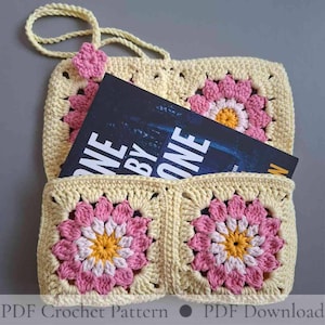 May include: A handmade crochet bag in a granny square design. The bag is cream-colored with pink and yellow flower motifs. A book with the title "ONE BY ONE" is inside the bag. The bag has a strap and a small flower accent.