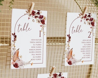 May include: Three table number cards with fall-themed floral designs and a list of names. The cards are numbered 1, 2, and 3. The cards are displayed on a gold wire stand.