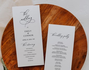 Pode incluir: Dois programas de cerimônia de casamento em uma bandeja de madeira com vegetação. Os programas são brancos com texto preto, incluindo os nomes "Emily & Connor" e a data "15 de abril de 2021". Um programa lista os detalhes da cerimônia, o outro a lista de convidados.