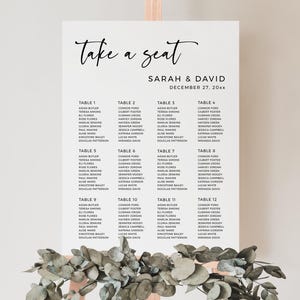 May include: A white wedding seating chart with black text. The chart is titled "Take a Seat" and lists the names of guests assigned to each table. The wedding date is listed as December 27, 20xx.