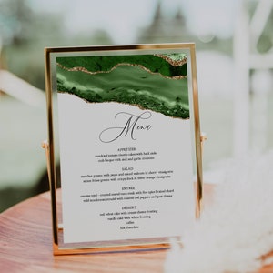 May include: A green and gold menu card with a marble-like design. The menu lists appetizers, salad, entree, and dessert options. The text reads: "Menu, Appetizer, Sundried tomato risotto cakes with basil aioli, Crab bisque with aioli and garlic croutons, Salad, Mesclun greens with pears and spiced walnuts in sherry vinaigrette, Mixes frisee greens with crispy duck in bitter orange vinaigrette, Entree, Sesame seed - crusted seared tuna steak with five spice braised chard, Wild mushroom strudel with roasted red peppers and goat cheese, Dessert, Red velvet cake with cream cheese frosting, Vanilla cake with white frosting, Coffee, Hot chocolate."