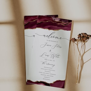 May include: A wedding ceremony program with a burgundy and gold agate design. The program includes the names Javier Flores and Luy White, the date April 15, 2021, and the ceremony order.