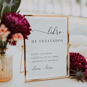 May include: A gold-edged sign with the word "libro" at the top, followed by "DE INVITADOS". The sign includes the text "HAZTE UNA FOTO, COLÓCALA EN EL LIBRO. ¡DEJANOS UN MENSAJE!" and the names "olivia + lucas".