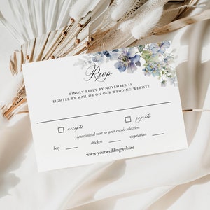 Puede incluir: Una tarjeta RSVP blanca con detalles florales azules. El texto dice "Reup" y "Por favor, responda antes del 15 de noviembre, por correo o en nuestro sitio web de bodas". La tarjeta incluye una casilla de verificaci&oacute;n para "acepta" y "lamenta" con un espacio para inicializar junto a su selecci&oacute;n de entrada: carne de res, pollo o vegetariano. La tarjeta tambi&eacute;n incluye la direcci&oacute;n del sitio web: www.yourweddingwebsite.