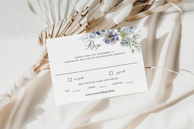 Puede incluir: Una tarjeta RSVP blanca con detalles florales azules. El texto dice "Reup" y "Por favor, responda antes del 15 de noviembre, por correo o en nuestro sitio web de bodas". La tarjeta incluye una casilla de verificaci&oacute;n para "acepta" y "lamenta" con un espacio para inicializar junto a su selecci&oacute;n de entrada: carne de res, pollo o vegetariano. La tarjeta tambi&eacute;n incluye la direcci&oacute;n del sitio web: www.yourweddingwebsite.